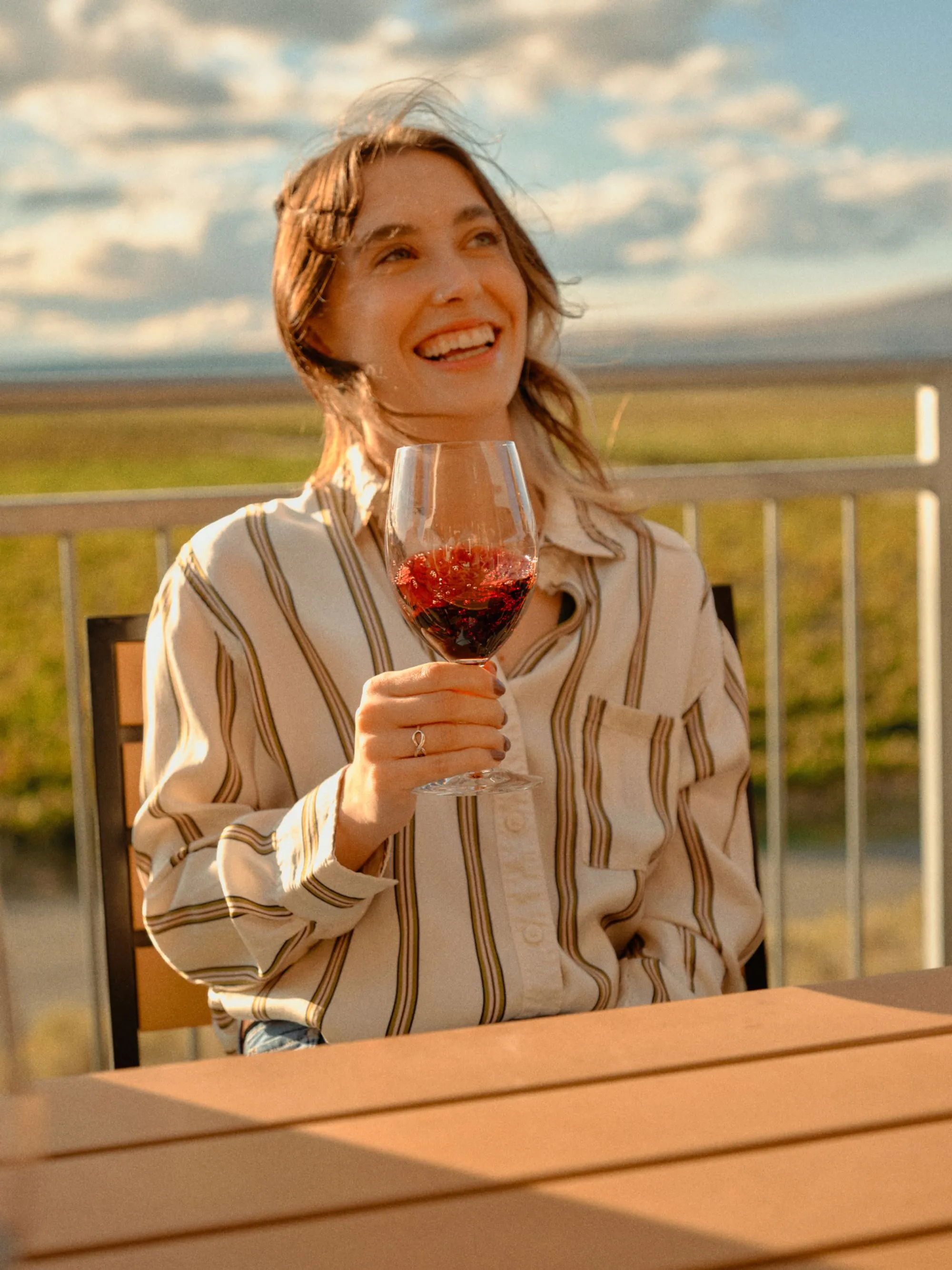 A woman smiling holding a glass of wine sitting at a table outside