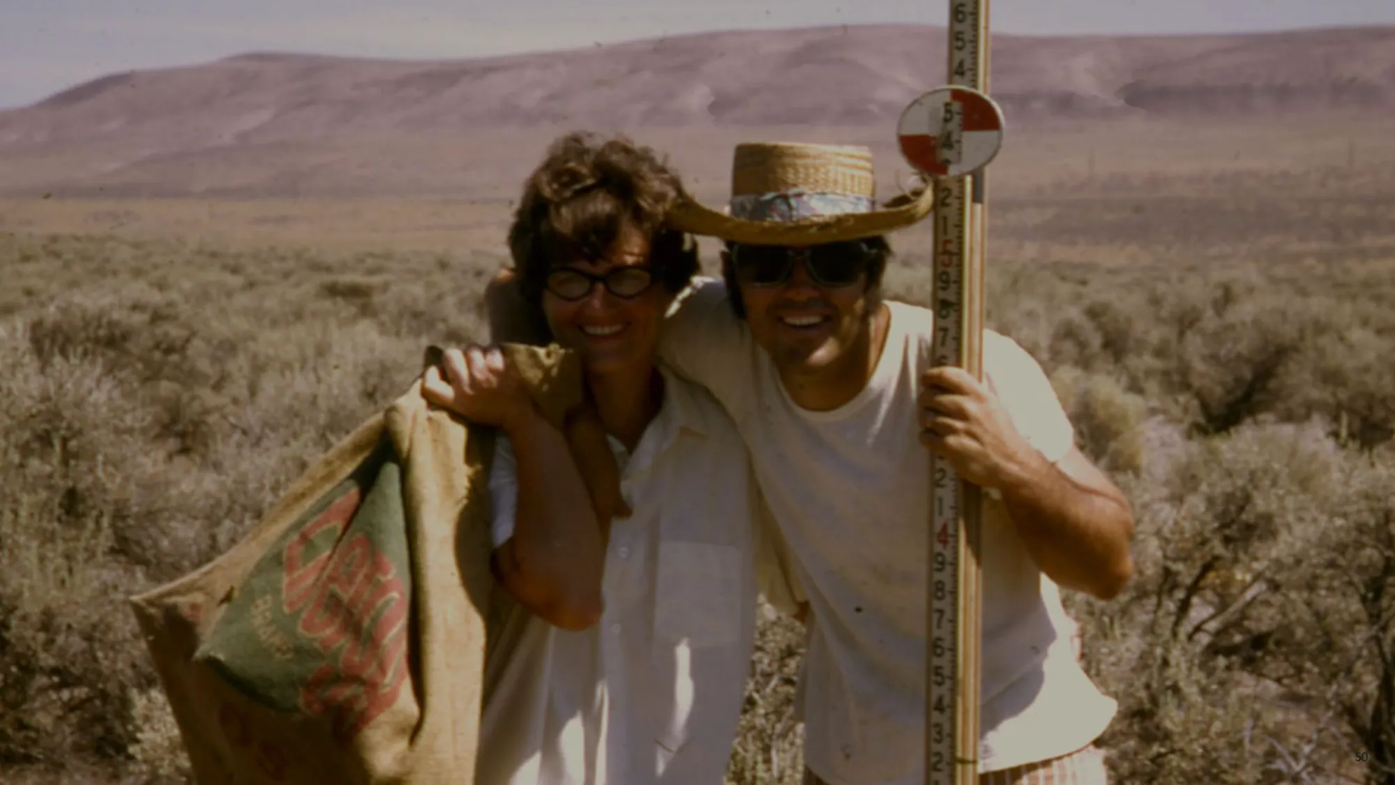 Vintage photo of two people in work clothes smiling in an arid landscape.