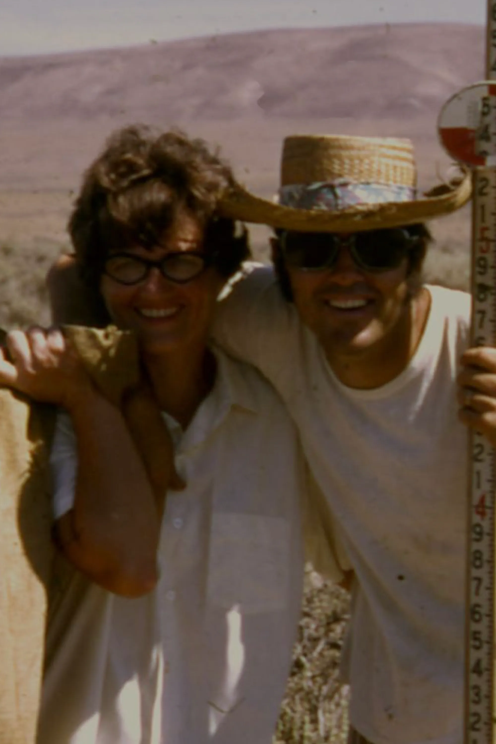 Vintage photo of two people in work clothes smiling in an arid landscape.